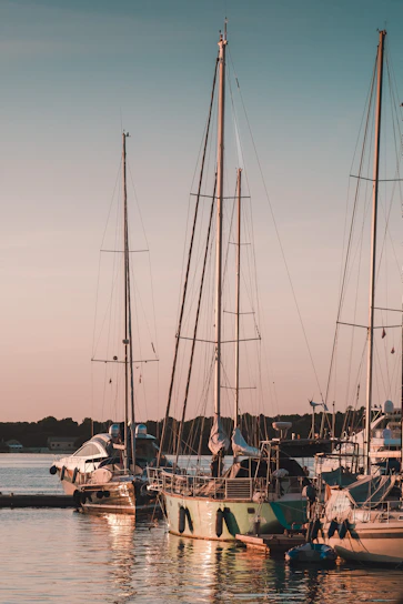 A serene blue sky over a marina with yachts docked and a glowing sunset reflecting on the water.