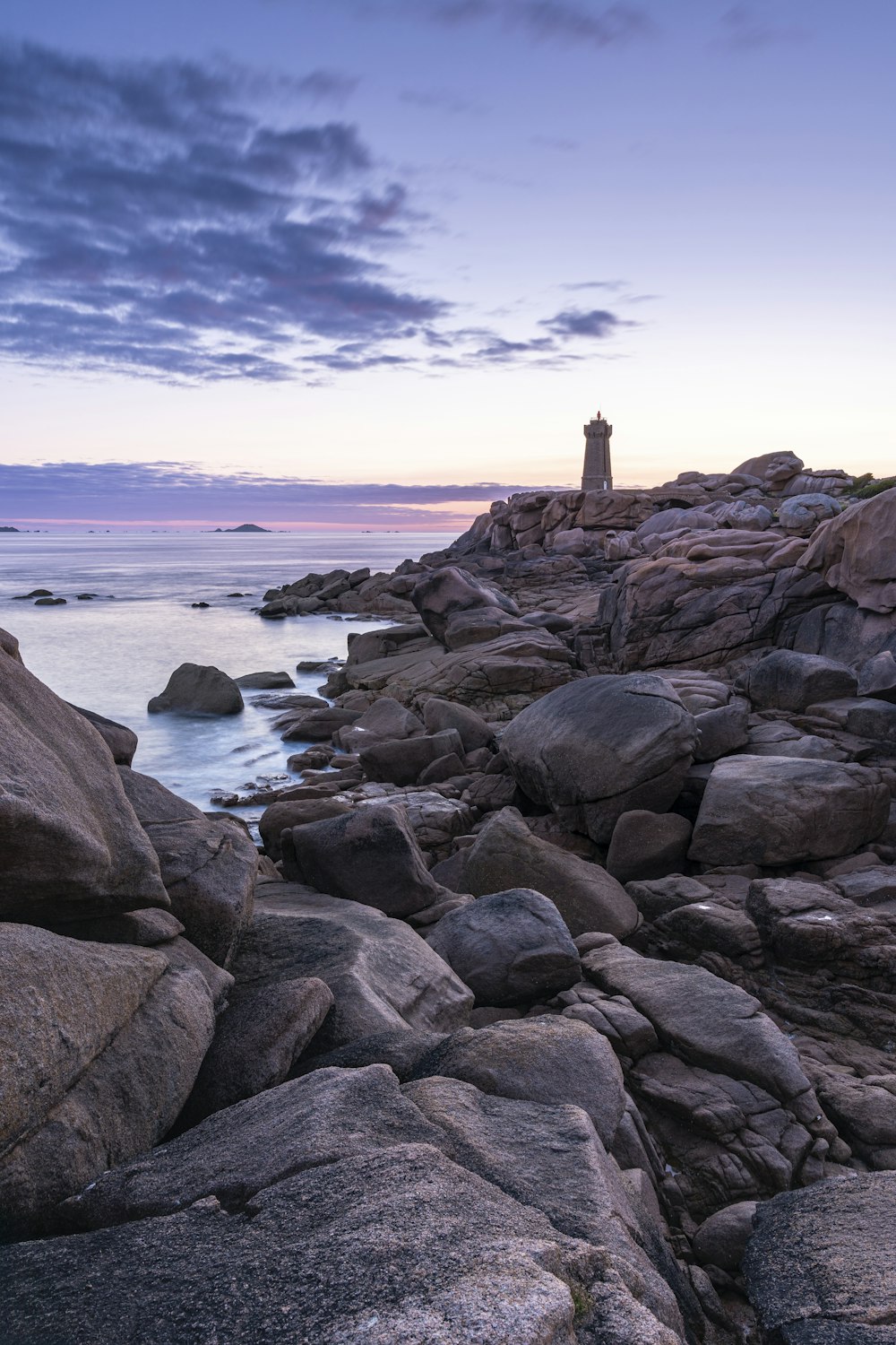 Un phare sur une rive rocheuse au coucher du soleil
