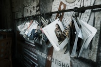 A series of fashion magazines hanging from hooks on a metal rod, with a focus on magazine covers that display models and fashion branding. The backdrop features a mosaic wall design with abstract patterns.
