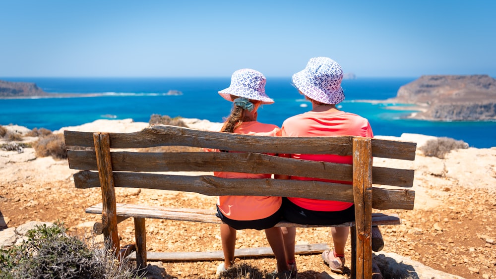 duas mulheres sentadas em um banco olhando para o oceano
