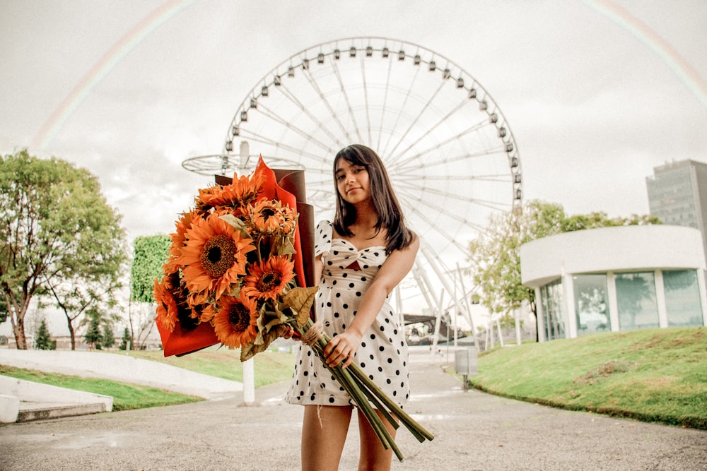 a woman holding a bouquet of sunflowers in front of a ferris wheel