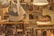 A cozy workshop setting with various leather goods and accessories on display. Handcrafted items such as wallets, bags, and keychains are neatly arranged on a wooden table. There is a sewing machine in the background, along with hanging lamps that provide warm lighting. The ambiance suggests a focus on craftsmanship and artisanal work.