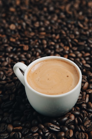 A steaming cup of Ace Brew coffee with coffee beans scattered around on a clean white surface.