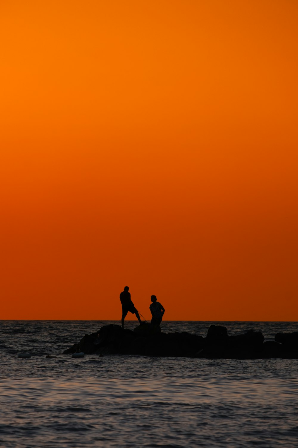 a couple of people standing on top of a rock in the ocean