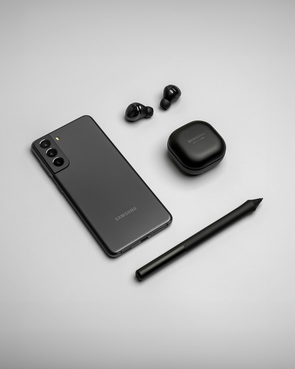 a black samsung phone, ear buds, and a black pen