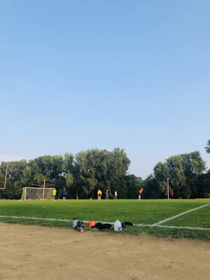 Kids and adults engaged in a friendly soccer match on the green field surrounded by trees.