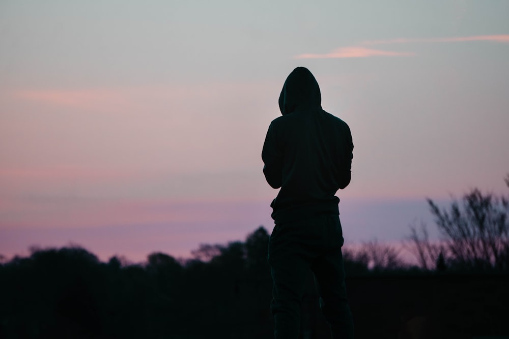 a silhouette of a person in a hoodie looking at the sky