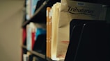 A close-up view of a collection of files or magazines in a library or archive setting. The focus is on a publication titled 'Tributaries' with visible shelves holding other documents in the background. The lighting creates a slightly nostalgic, quiet atmosphere.