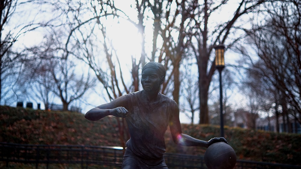 a statue of a man holding a ball in a park