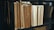 A collection of old, worn folders and files are neatly arranged on a dark shelf. The edges of the papers are yellowed, indicating age, and the surface of the shelf is a deep black, providing contrast to the light-colored documents.