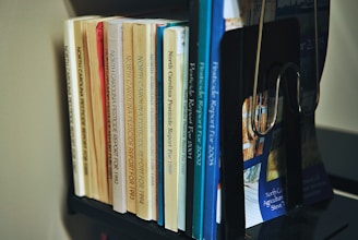 A collection of books organized on a shelf. The books are primarily reports on North Carolina pesticides, with publication years ranging from the early 1990s to the early 2000s. The books vary in color, including shades of yellow, orange, blue, and white. A black bookend supports them, and the titles are clearly visible.