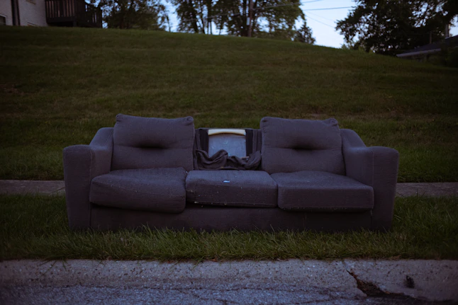 A friendly ecorydas team member lifting a couch out of a sunny living room, with a recycling truck in the background.
