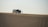 A group of people stands near an SUV with an open hood on a vast sand dune, suggesting a possible car breakdown or rest stop. The sand has smooth, wavy patterns, and the sky is clear.
