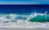A vertical video still of waves crashing on a bright sunny beach.