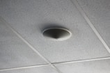 A ceiling with acoustic tiles arranged in a grid pattern and a round speaker or smoke detector mounted in the center of one tile.