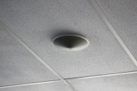 A close-up of a smoke detector on a ceiling.