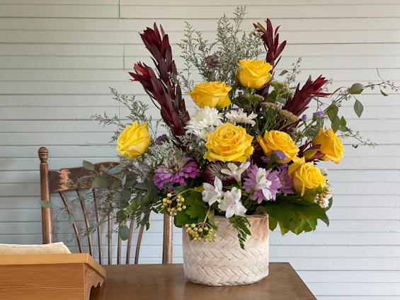 A vibrant floral arrangement featuring soft green, lilac, and yellowish-green hues on a rustic wooden table.
