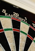 A close-up of a dartboard featuring sections marked with numbers 5, 20, and 1 on the top area. The dartboard has a traditional design with alternating black and cream segments, as well as red and green rings.