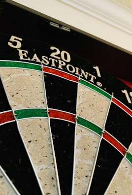 A close-up of a dartboard featuring sections marked with numbers 5, 20, and 1 on the top area. The dartboard has a traditional design with alternating black and cream segments, as well as red and green rings.