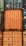 A stack of intermodal shipping containers featuring prominent brand labeling and identification numbers. The containers display various colors, primarily orange, blue, and green, and they are arranged in a grid-like formation. The surfaces show signs of weathering and rust, indicating frequent use and exposure to the elements.