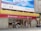 A bank building with signage for CMB Wing Lung Bank, featuring a large red and yellow sign with Chinese and English text. Several people are walking on the sidewalk in front of the building, and there are decorative stone lions by the entrance. Above the bank is a large blue and white advertisement billboard with cityscape graphics.