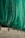 A large green net or fabric is draped over a series of black metal supports attached to a beige corrugated wall. The net hangs in loose folds, partially covering the supports and casting shadows on the wall.