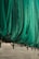 A large green net or fabric is draped over a series of black metal supports attached to a beige corrugated wall. The net hangs in loose folds, partially covering the supports and casting shadows on the wall.