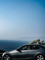 Rear view of a compact hybrid car with a scenic ocean backdrop under clear skies.