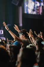 A vibrant crowd at a nighttime concert, hands raised under colorful stage lights.