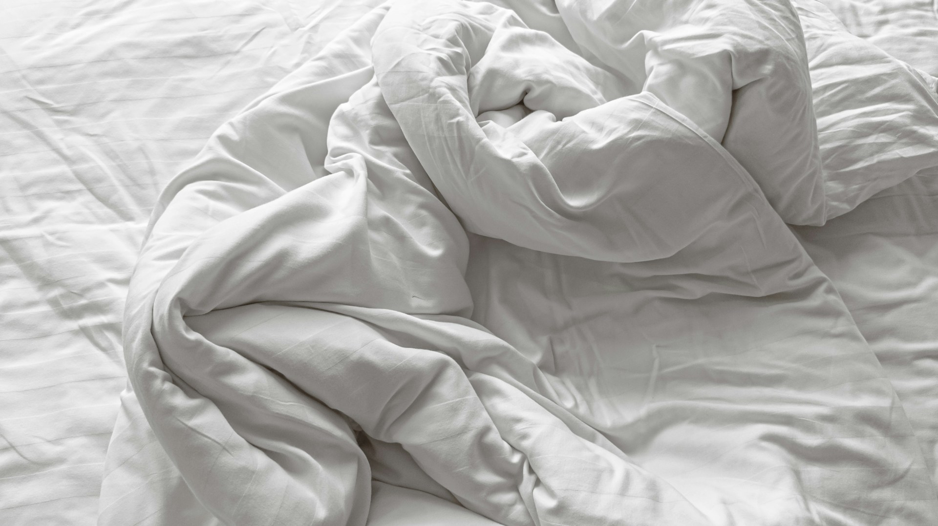 an unmade bed with white sheets and pillows