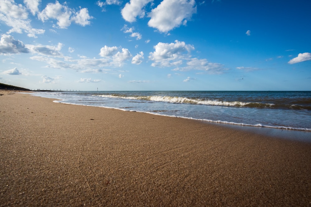 a sandy beach next to the ocean under a blue sky