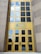 A tall building entrance with large yellow-framed glass doors and windows. The logo of Standard Chartered is prominently displayed above the doors. The reflection in the windows shows a blue sky with white clouds.