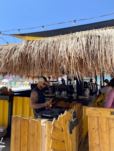 A cozy beachfront restaurant with people practicing morning yoga and a DJ playing electronic music at sunset.