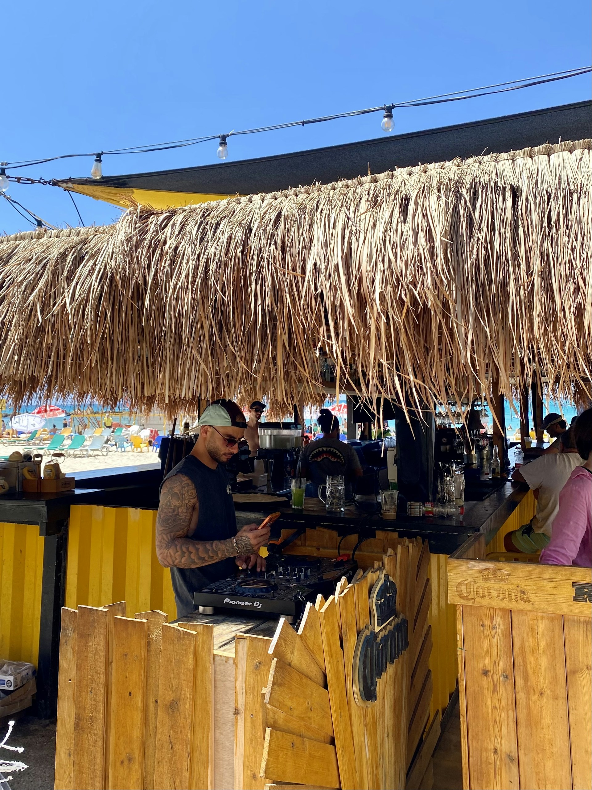 A vibrant DJ booth on a tropical beach at sunset, with colorful lights reflecting the Afro Caribbean house vibe of The Barth's Brothers.