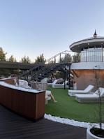 A rooftop terrace covered with artificial grass, decorated with potted plants and wooden furniture.