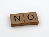 Two wooden Scrabble tiles are placed side by side. The tiles display the letters 'N' and 'O' respectively, both with a value of 1 point.