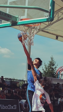 Young basketball players in blue and orange jerseys competing passionately on an outdoor court.