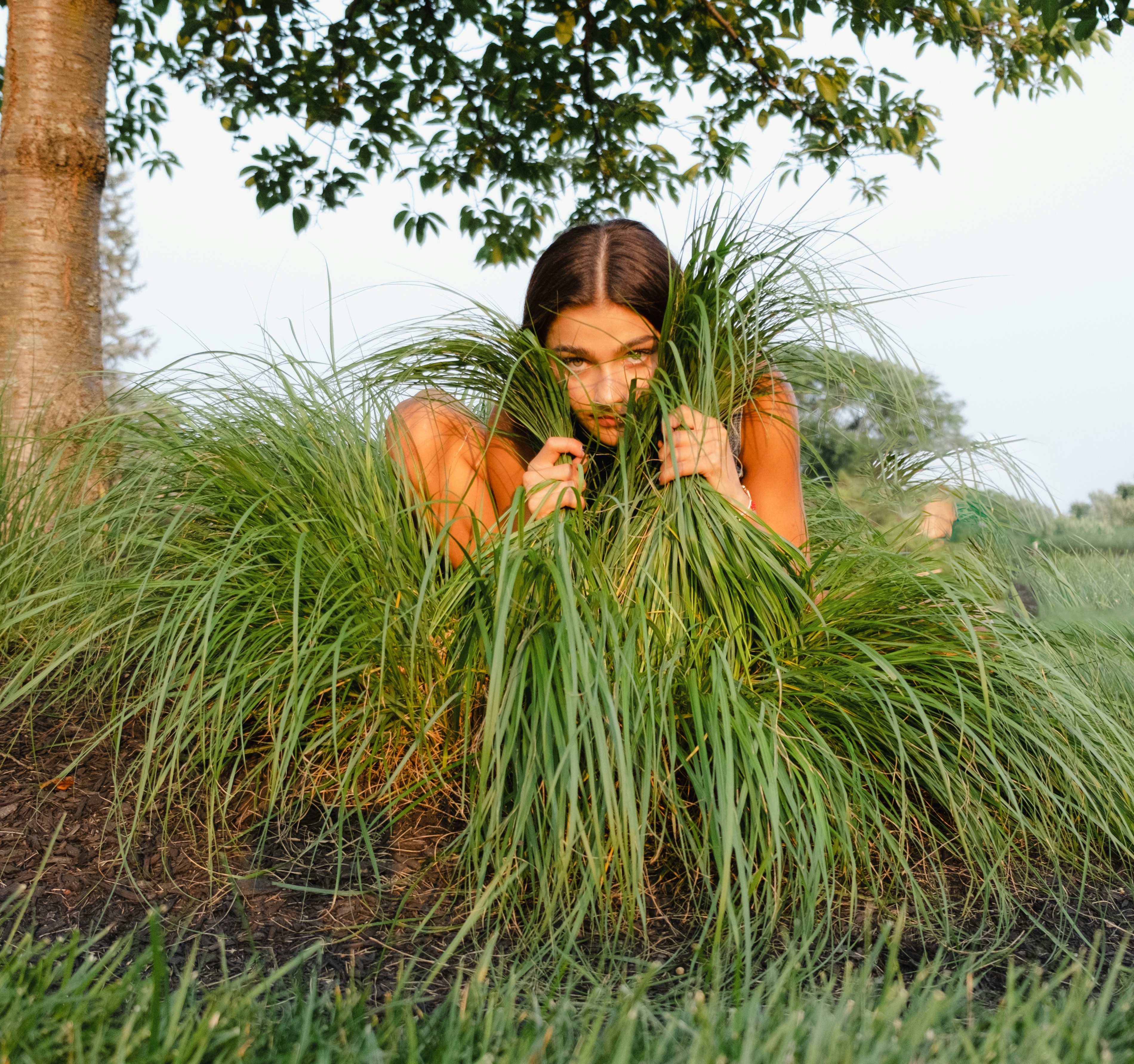 a woman is hiding behind some tall grass