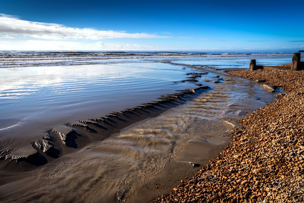 a sandy beach next to the ocean under a blue sky