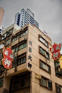 A building with traditional Chinese signage and architectural features, surrounded by other high-rise structures. The sky appears overcast, adding a muted tone to the scene. The signs are prominently displayed in bright red and gold colors with stylized characters.