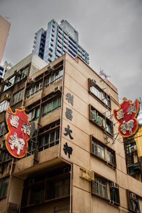 A building with traditional Chinese signage and architectural features, surrounded by other high-rise structures. The sky appears overcast, adding a muted tone to the scene. The signs are prominently displayed in bright red and gold colors with stylized characters.