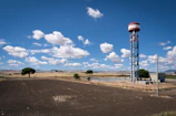 Water tower installed near a farmhouse surrounded by fields and construction equipment.