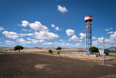 Water tower installed near a farmhouse surrounded by fields and construction equipment.