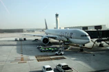 A ground crew member guiding a large commercial aircraft on the tarmac under a clear blue sky.