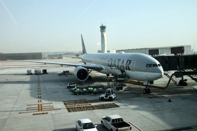 A ground crew member guiding a large commercial aircraft on the tarmac under a clear blue sky.