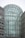 A modern architectural structure with a large glass atrium. The design features intricate geometric patterns made from black metal frames and transparent glass panels. Surrounding the atrium are stone-clad buildings with windows, creating a balance between glass and solid materials.