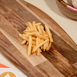 Golden fries arranged neatly on a rustic wooden board with a sprinkle of herbs.