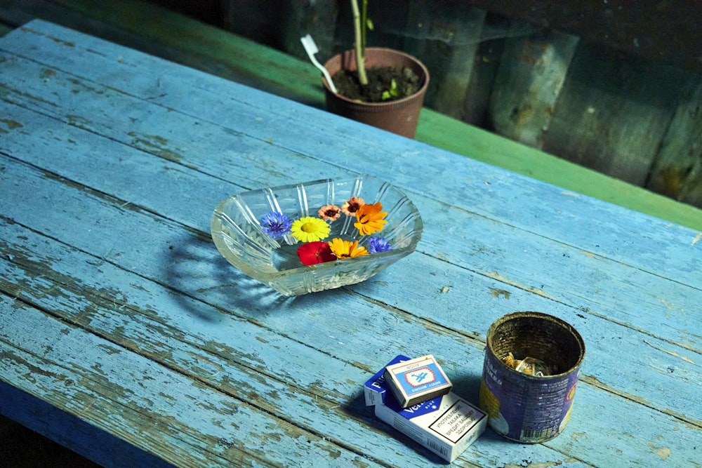 a glass bowl of flowers sitting on top of a wooden table