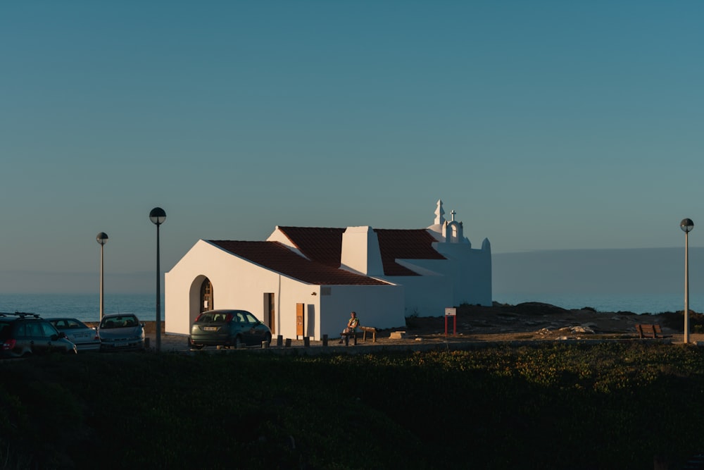a white church with a red roof next to the ocean