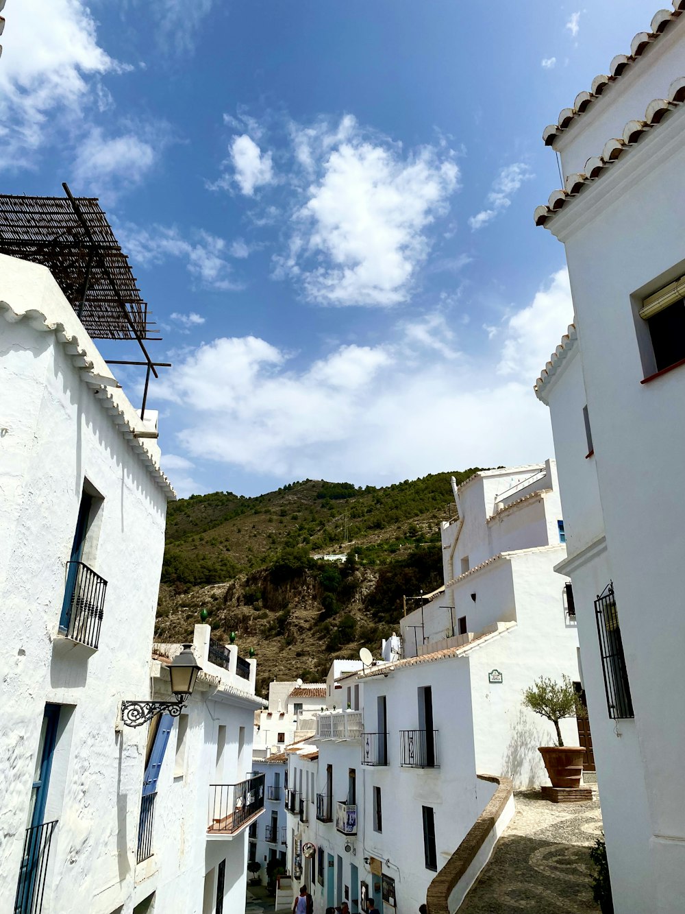 a narrow street with white buildings and a hill in the background